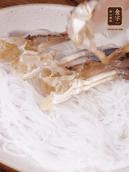 盤底墊上粉絲，擺上梭子蟹、火腿片，撒姜粒，淋上蒸魚豉油、花雕酒調(diào)味腌制15分鐘